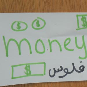 Handmade sign in classroom that says "money" in English and Arabic